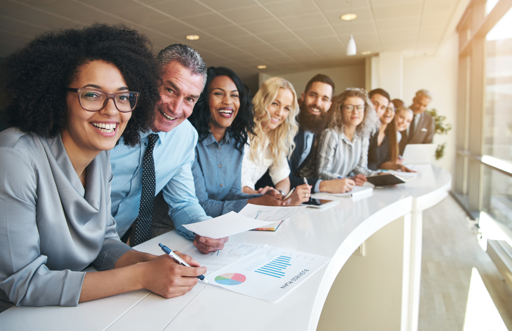 Group of smiling employees leaning against curved conference table